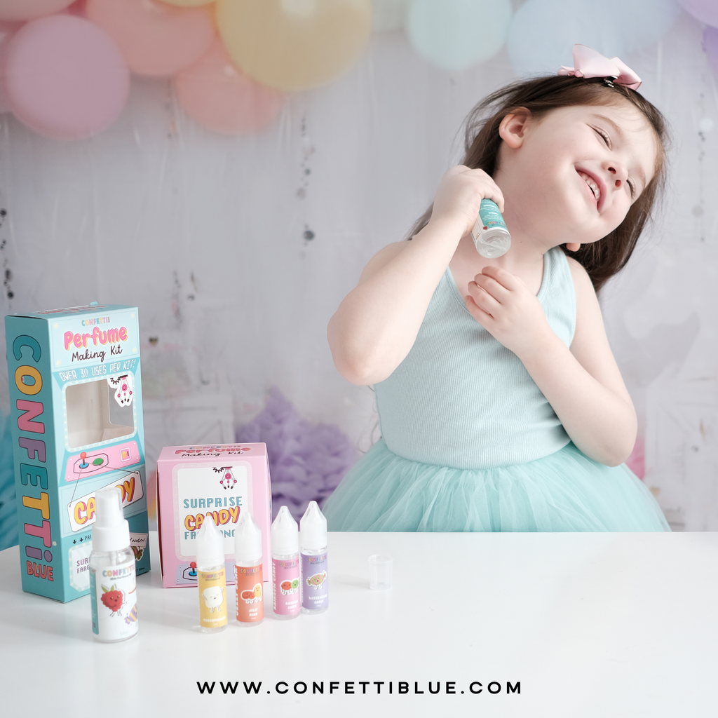 5 year old girl with blue shirt and pink bow holding a Confetti Blue Candy Scented Perfume Making Kit for Kids spraying perfume on her after birthday