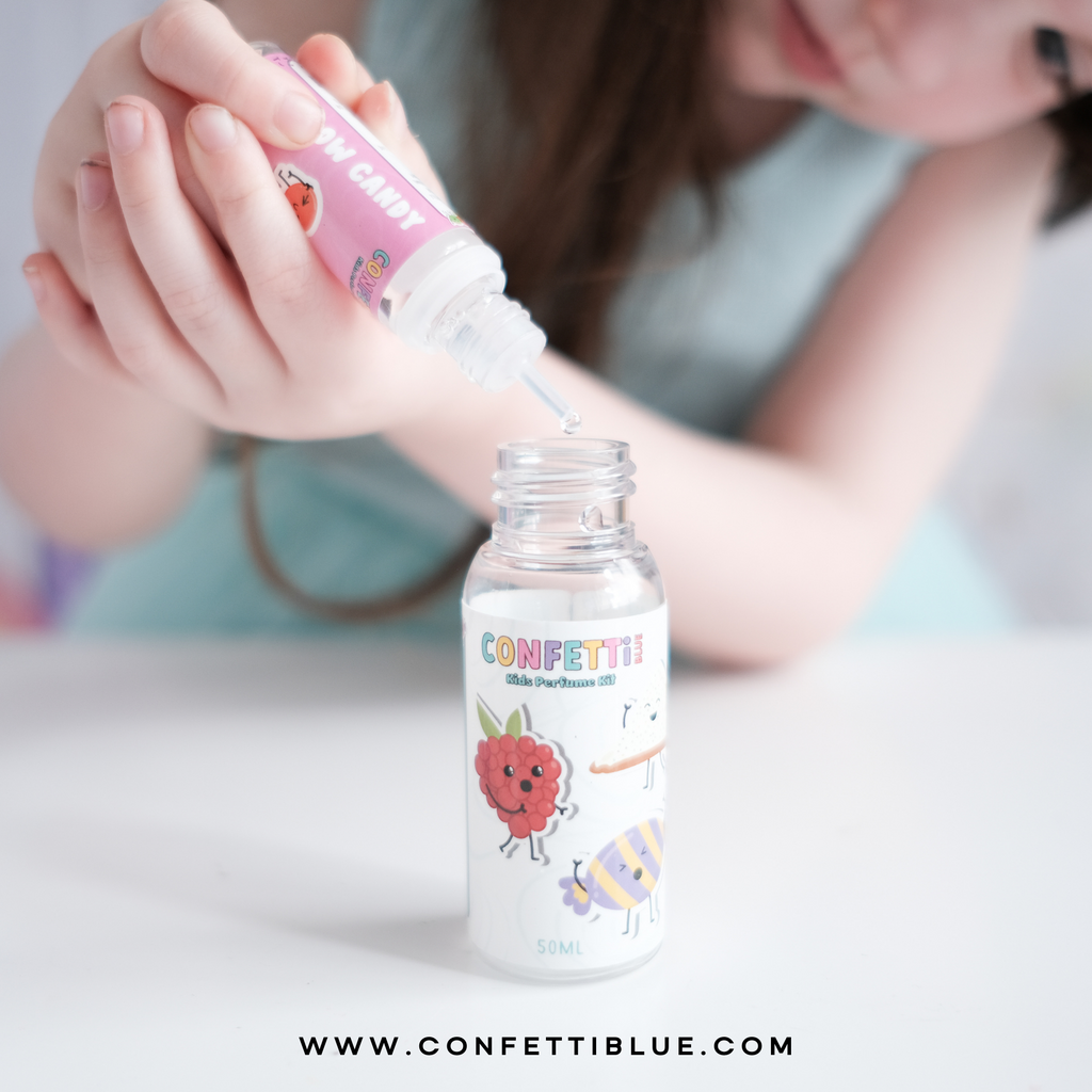 Confetti Blue Kids Perfume. Little Girl with blue shirt and pink bow holding a Confetti Blue Candy Scented Perfume Making Kit for Kids mixing her perfume