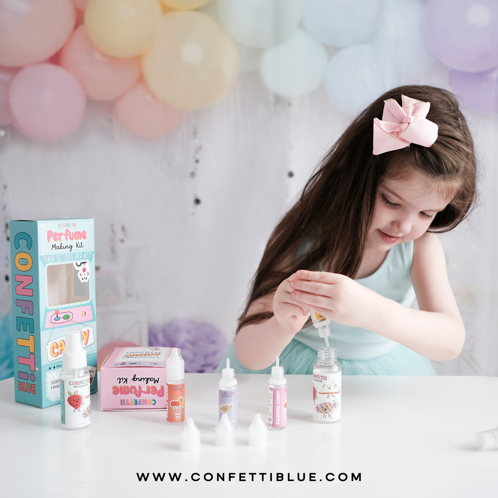 Confetti Blue Kids Perfume. Little Girl with blue shirt and pink bow holding a Confetti Blue Candy Scented Perfume Making Kit for Kids mixing her perfume together